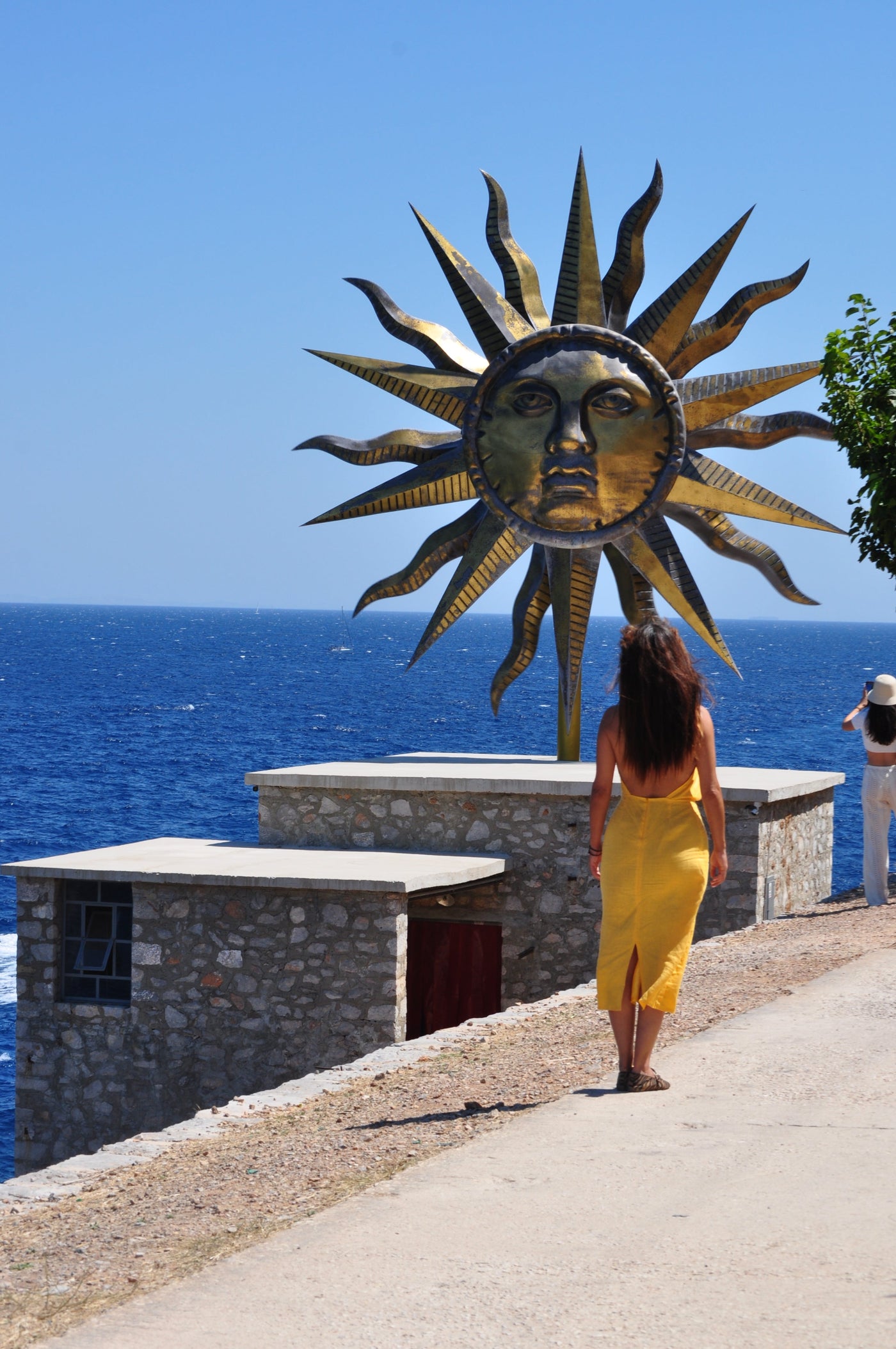 Eleanna Tabouri, Creative Director of Nevro Blazer, infant of the Jeff Koons installation Apollo Sun in Hydra wearing the new SS27 Yellow linen Nevro Blazer Dress 