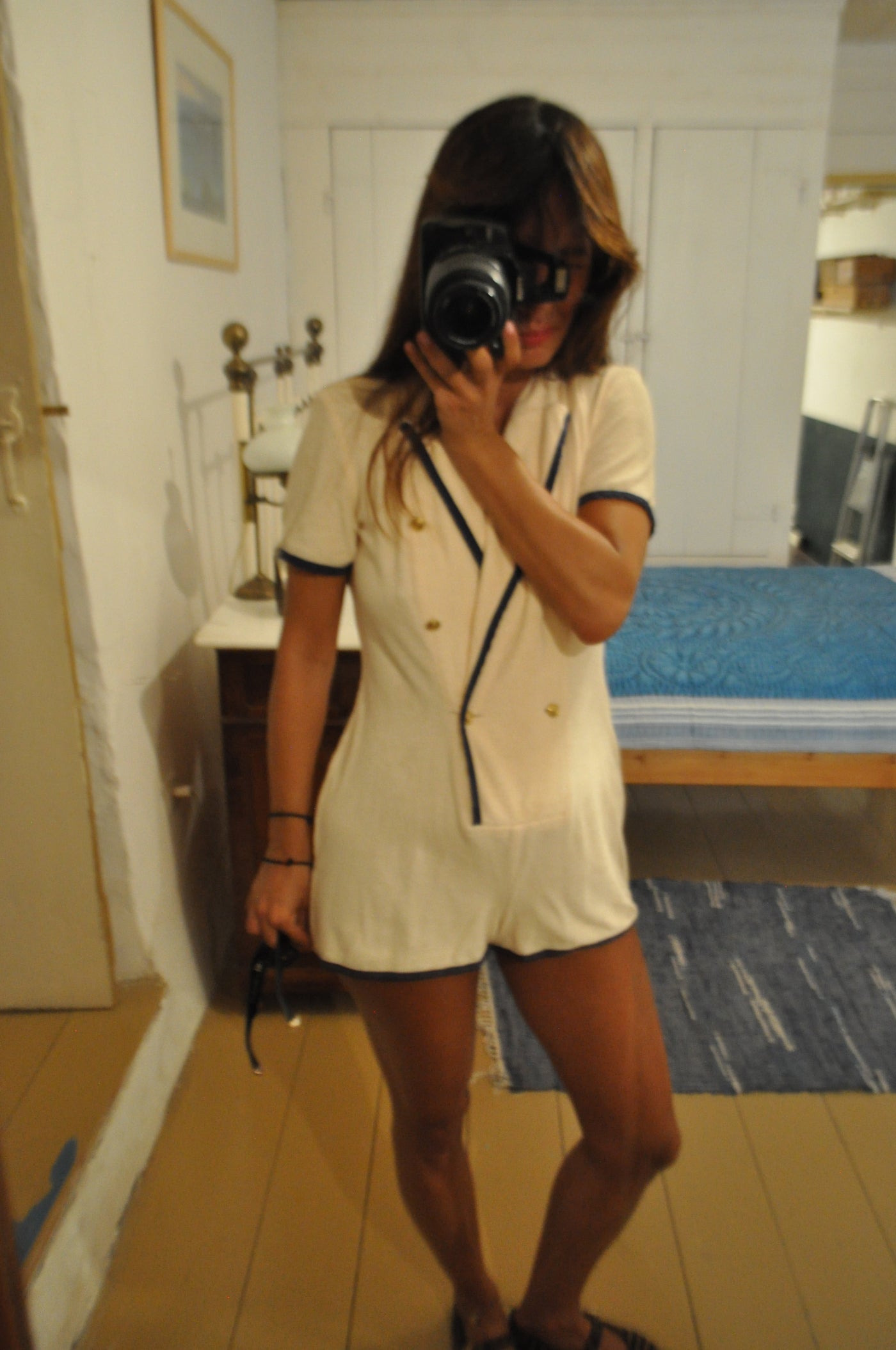 Eleanna Tabouri, Creative Director of Nevro Blazer  taking a mirror selfie in a bedroom, wearing a Terry cream-colored playsuit with dark trim and gold buttons from SS collection Nevro Blazer