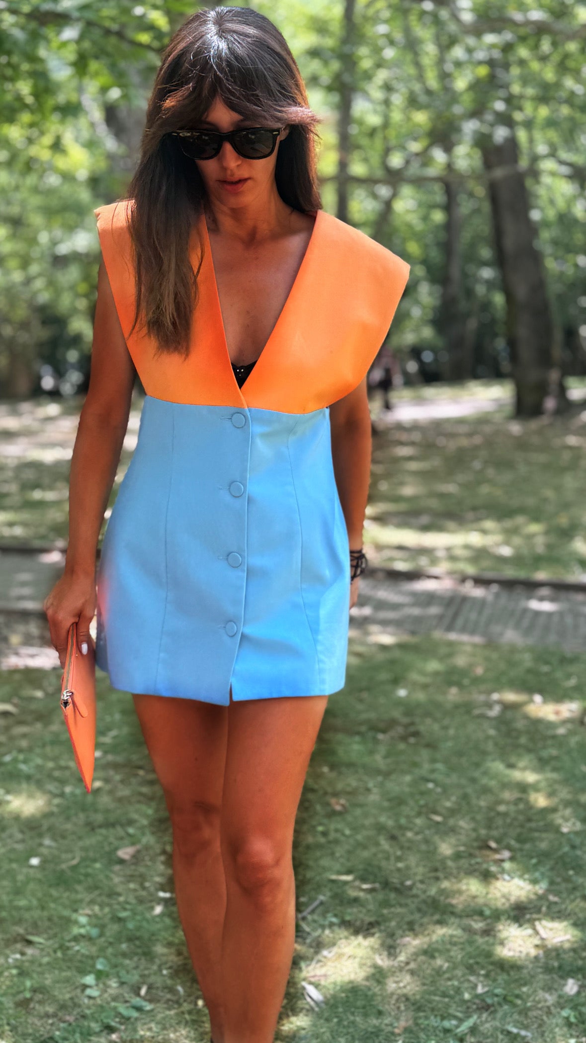 Eleanna Tabouri wearing the spritz color-block nevro blazer mini dress with a bright orange yoke and a light blue skirt with front buttons, walking in a park.