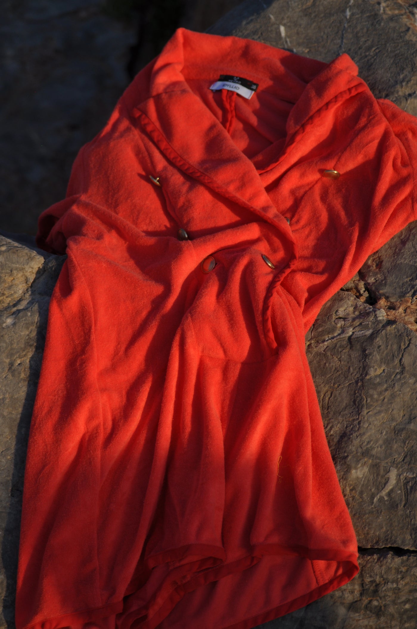 A bright red Terry shawl collar top with gold buttons, laid out on a dark textured stone surface.